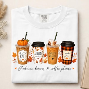 May include: A white t-shirt featuring a graphic of four coffee cups with autumn themes. The cups display the text "hello FALL", "AUTUMN vibes", "SWEATER WEATHER", and "Pumpkin SPICE". Below the cups, the text reads "Autumn leaves & coffee please".
