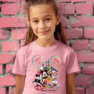 May include: Pink t-shirt featuring a Disney family vacation design. The graphic includes Mickey and Minnie Mouse, Donald and Daisy Duck, Goofy, and Pluto. The shirt has the text "2026" and "Name" in a Mickey Mouse ear design.