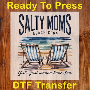 May include: DTF Transfer with the text "Ready To Press". The design features two beach chairs with blue and white stripes, the words "Salty Moms Beach Club", and the phrase "Girls just wanna have Sun". The background shows a beach scene.