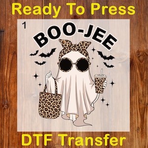 May include: A DTF transfer featuring a cartoon ghost with sunglasses, a leopard print headband, and a matching tote bag and coffee cup. The text "BOO-JEE" is above the ghost, with "Ready To Press" and "DTF Transfer" at the top and bottom.