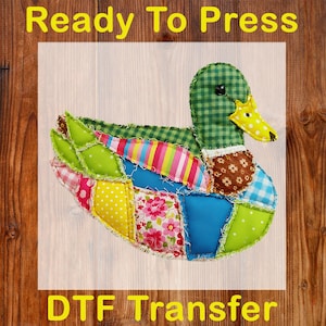 May include: A colorful, patchwork duck design with a green checkered head and a yellow beak. The duck's body is made of various fabric patterns, including polka dots, stripes, and floral prints. The text "Ready To Press" and "DTF Transfer" are displayed.