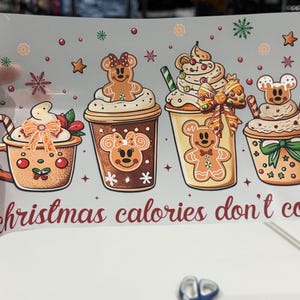 Op de afbeelding: Een feestelijke illustratie met vier drankjes met een vakantiethema. Elk drankje is versierd met slagroom, peperkoekfiguren en feestelijke decoraties. De zin "christmas calories don't count" staat in rode letters.