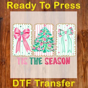May include: A DTF transfer design with three rectangular frames. The frames feature a pink bow, a Christmas tree, and a floral bow, all on a striped background. The text "TIS THE SEASON" is below the frames.