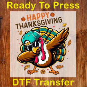 Puede incluir: Una transferencia DTF con un pavo de dibujos animados con gafas de sol y una gorra turquesa, con el texto "Happy Thanksgiving" y "Ready To Press". El pavo es marrón, rojo y amarillo, con una cola turquesa y amarilla. Hojas de otoño y estrellas rodean al pavo.