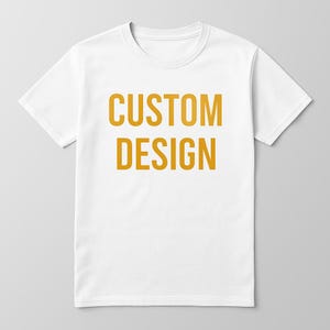 May include: White t-shirt with the words "CUSTOM DESIGN" printed in a bold, orange font. The shirt has a crew neck and short sleeves. The design is centered on the front of the shirt.