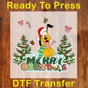 May include: A DTF transfer featuring Pluto in a Santa hat and scarf, with the text "MERRY CHRISTMAS". The design includes Christmas trees, snowflakes, candy canes, and gift boxes. The words "Ready To Press" and "DTF Transfer" are also displayed.