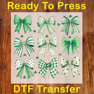 Puede incluir: Una lámina con nueve diseños de lazos verdes con varios patrones, incluyendo lunares, rayas y cuadros, con detalles de tréboles. El texto "Ready To Press" y "DTF Transfer" se muestra en amarillo.