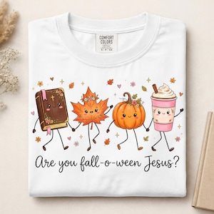 May include: A white t-shirt featuring a graphic of a cartoon book, maple leaf, pumpkin, and coffee cup holding hands. The text "Are you fall-o-ween Jesus?" is printed below the characters. The shirt has a Comfort Colors brand label at the neck.