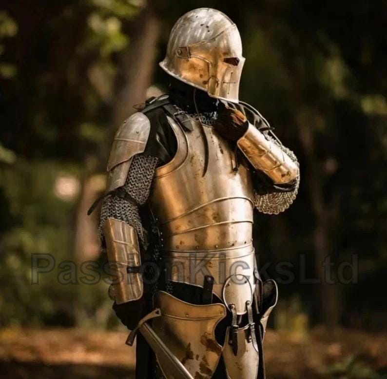 Puede incluir: Una armadura medieval completa en tono dorado, que incluye un yelmo, peto y protecci&oacute;n para brazos y piernas. La armadura se lleva sobre una prenda oscura, con cota de malla visible en las articulaciones. El fondo es un bosque borroso.