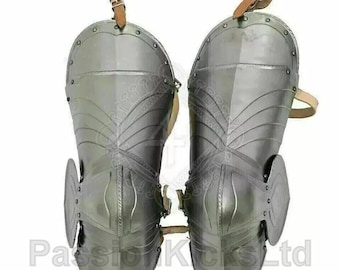 May include: Pair of polished steel medieval leg armor. Each piece features riveted construction, articulated plates, and leather straps with buckles for attachment. The armor is designed to protect the knees and shins.