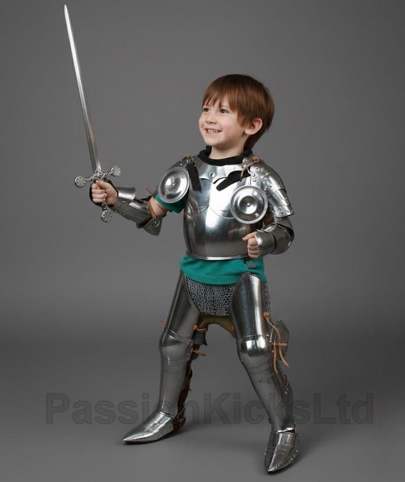 May include: A child in a full suit of shiny, silver-colored knight's armor, including a breastplate, arm and leg guards, and a helmet. The child is holding a silver sword and smiling. The armor is detailed and realistic, creating a medieval theme.