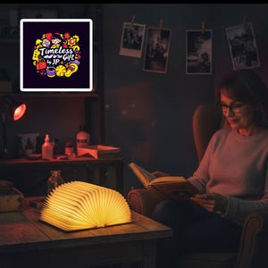 May include: A warm, glowing book-shaped lamp sits on a wooden table, illuminating the room. The lamp is open, with the pages fanned out. A woman is reading a book in a chair. A framed image with the text "Timeless Gift by JP" hangs on the wall.