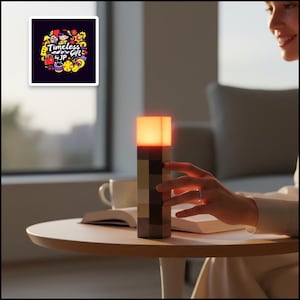 Könnte beinhalten: Rechteckige Lampe mit warmem, orangefarbenem Licht. Der Lampenkörper ist farblich in Braun- und Beigetönen abgesetzt. Der Text "Timeless Gift by JP" ist auf einem Aufkleber im Hintergrund zu sehen.