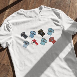 May include: White t-shirt featuring a collection of colorful, illustrated t-shirts. Each miniature shirt has a unique design, including various colors and patterns. The shirts are arranged on the front of the white tee.