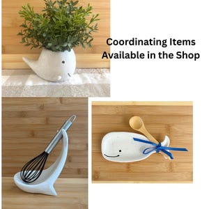 May include: A collection of kitchen decor items, including a whale-shaped planter with greenery, a whisk with a matching holder, and a whale-shaped spoon rest with a wooden spoon and blue ribbon. The text "Coordinating Items Available in the Shop" is also visible.