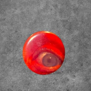 May include: A circular pinback button featuring a vibrant red background with a detailed, realistic photographic print of a human eye centered within the design. The eye has a visible iris and pupil, set against the bright red, glossy surface.