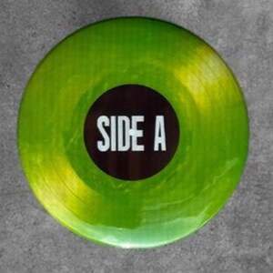 May include: A circular vinyl record featuring a translucent lime green and yellow marbled finish. The center of the record has a solid black circular label with the white text SIDE A printed in a bold, sans-serif font across the middle.