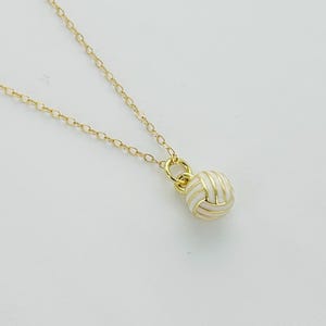 May include: A gold chain necklace with a small, round, gold pendant that has a knotted design.