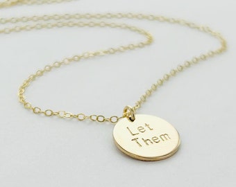 Puede incluir: Un collar de oro con un colgante redondo que dice "Let Them".