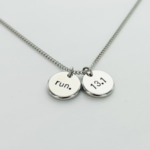 Puede incluir: Collar de plata con dos colgantes redondos. Un colgante dice "run." y el otro dice "13.1".