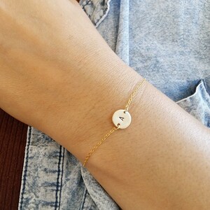 Könnte beinhalten: Ein zartes Armband aus einer goldenen Kette mit einem kleinen runden Anhänger mit dem Buchstaben 'A'.