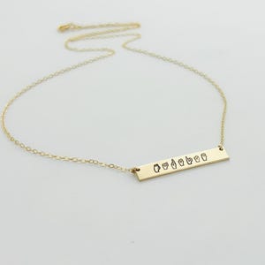 May include: Gold necklace with a bar pendant featuring the word "Love" spelled out in British Sign Language.