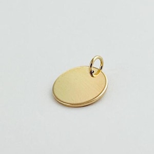 May include: A gold-colored round pendant with a smooth surface and a jump ring at the top.