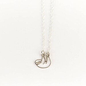 May include: A silver necklace with a sloth pendant. The sloth is hanging upside down with its arms and legs outstretched.