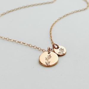 May include: A delicate gold necklace with two small, round pendants. One pendant features a floral design, the other a smaller floral motif. The fine chain adds elegance, suitable for daily wear. The necklace is gold-coloured.