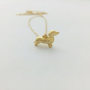 May include: A gold necklace with a dachshund pendant. The dachshund is standing on all four legs and has a long snout.
