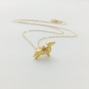 May include: A gold chain necklace with a small, gold dachshund pendant.