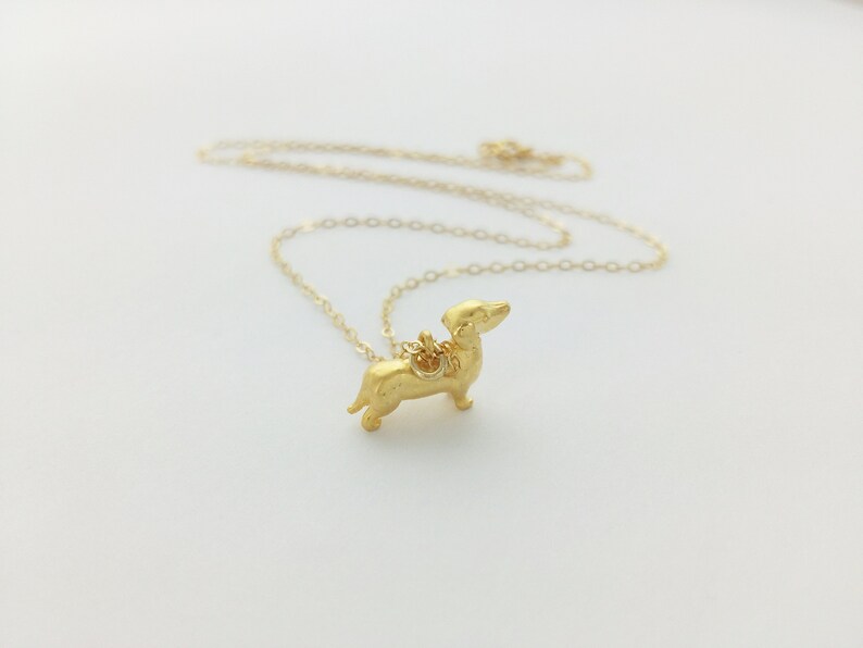 May include: A gold chain necklace with a small, gold dachshund pendant.