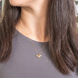 May include: A gold chain necklace with a small, delicate pendant shaped like a bird. The necklace is worn by a person with long brown hair.