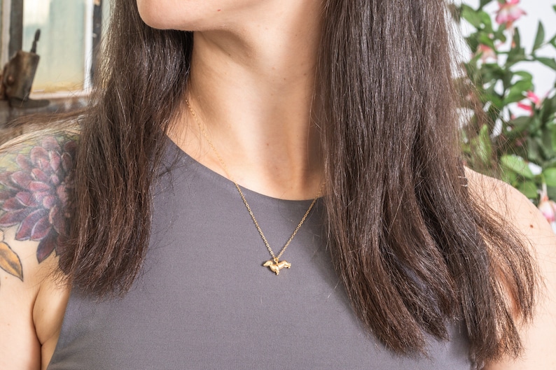 May include: A gold chain necklace with a small, delicate pendant shaped like a bird. The necklace is worn by a person with long brown hair.