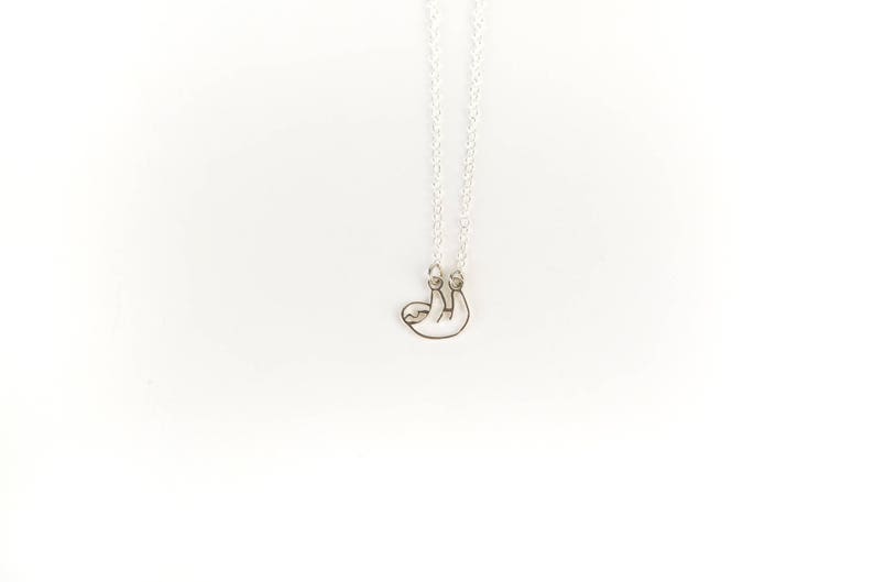 May include: A silver necklace with a sloth pendant. The sloth is hanging upside down with its arms and legs outstretched.