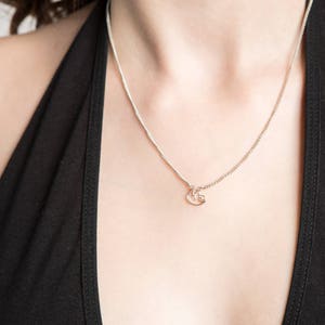 May include: A silver chain necklace with a small, delicate pendant. The pendant is shaped like a stylized letter 'G'.
