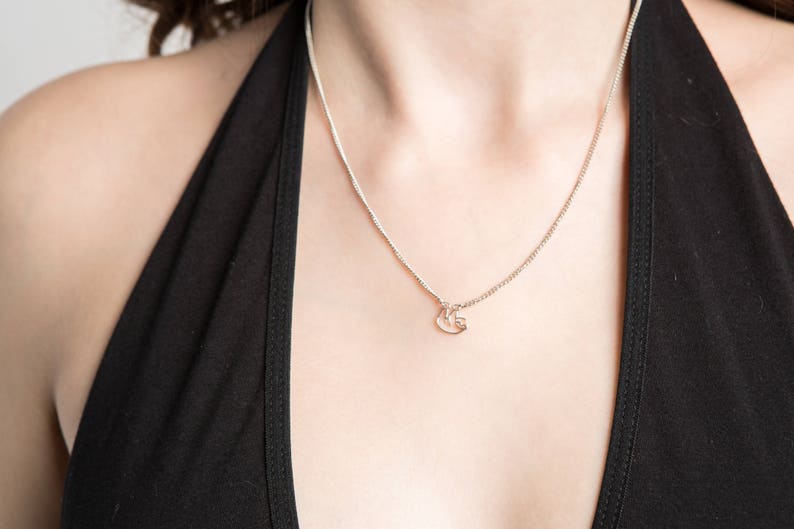 May include: A silver chain necklace with a small, delicate pendant. The pendant is shaped like a stylized letter 'G'.