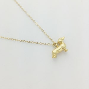 May include: A gold chain necklace with a small, gold dachshund pendant.