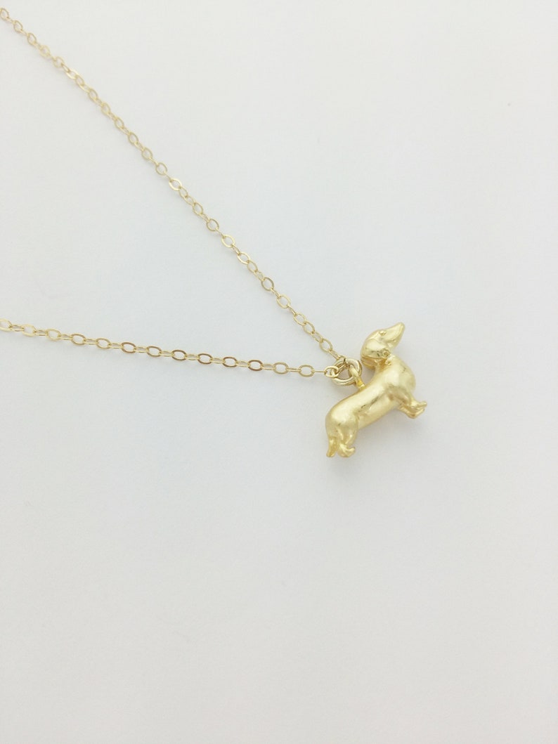 May include: A gold chain necklace with a small, gold dachshund pendant.