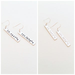 May include: Silver earrings with a rectangular charm featuring the coordinates "50.8647&deg;N 121.7376&deg;W" engraved on each charm.