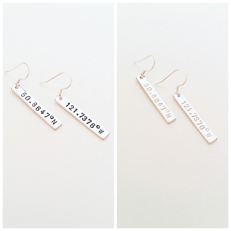 May include: Silver earrings with a rectangular charm featuring the coordinates "50.8647&deg;N 121.7376&deg;W" engraved on each charm.