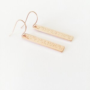 May include: Rose gold earrings with a bar design. Each bar has coordinates engraved on it: 45.27751.1596&deg;N and 9&deg;11'28.9778&deg;E.