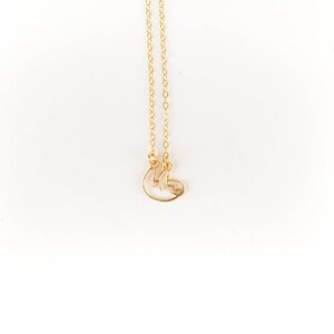 May include: A gold chain necklace with a delicate, wire-shaped sloth pendant.