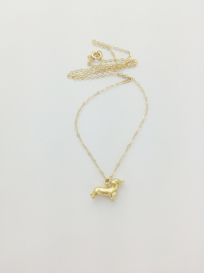 May include: A gold chain necklace with a small, gold dachshund pendant.