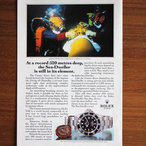 Puede incluir: Anuncio con buzos conectando una tubería bajo el agua. El texto destaca el reloj Rolex Sea-Dweller, enfatizando su precisión y fiabilidad a una profundidad de 520 metros.