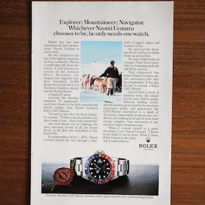 Könnte beinhalten: Werbung für eine Rolex GMT-Master Uhr mit schwarzem Zifferblatt und rot-blauer Lünette. Die Uhr wird vor weißem Hintergrund mit Text über den Entdecker Naomi Uemura gezeigt.