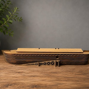 May include: A dark brown wooden model of a boat featuring a layered hull construction, a flat rectangular roof section, and a small triangular ramp structure attached to the side. The model displays visible horizontal wood grain and dark edges.