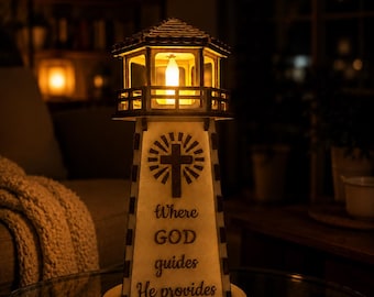 May include: A light-colored wooden lighthouse lamp with a glowing interior light. The front features a dark brown cutout of a cross surrounded by rays and the text "Where GOD guides He provides" in a dark brown script font on the main body.