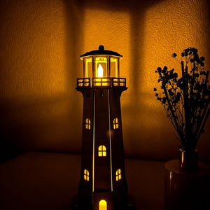 May include: A vertical lighthouse lamp featuring a light-colored structure with multiple arched windows and a lantern room at the top. The lamp emits a warm, glowing yellow light from within, casting a bright illumination through the openings.