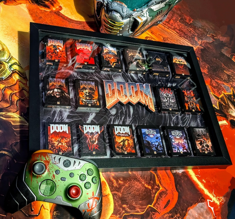 Op de afbeelding: Een ingelijste display met meerdere DOOM game cases, met een groot DOOM logo in het midden. Een aangepaste groene en rode Xbox controller staat op de voorgrond. De achtergrond heeft een oranje en zwart thema.
